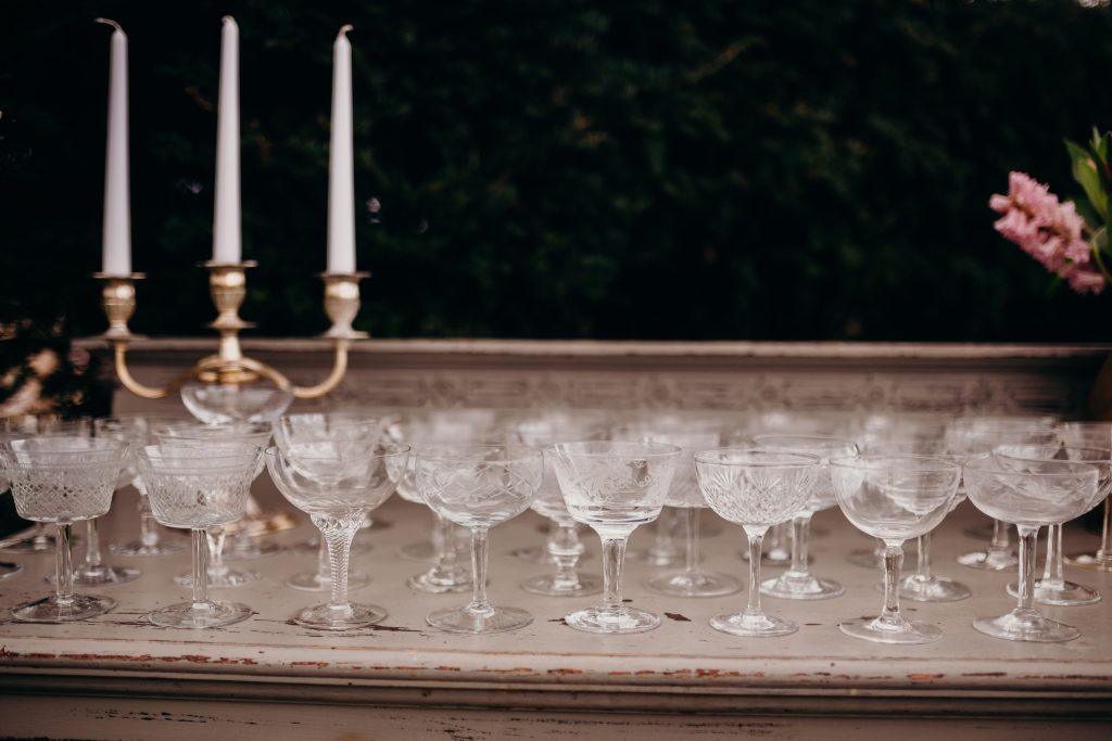 a cocktail bar with vintage cut crystal champagne saucers on top and a beauty and the beast style candelabra with three white tapered candles to hire