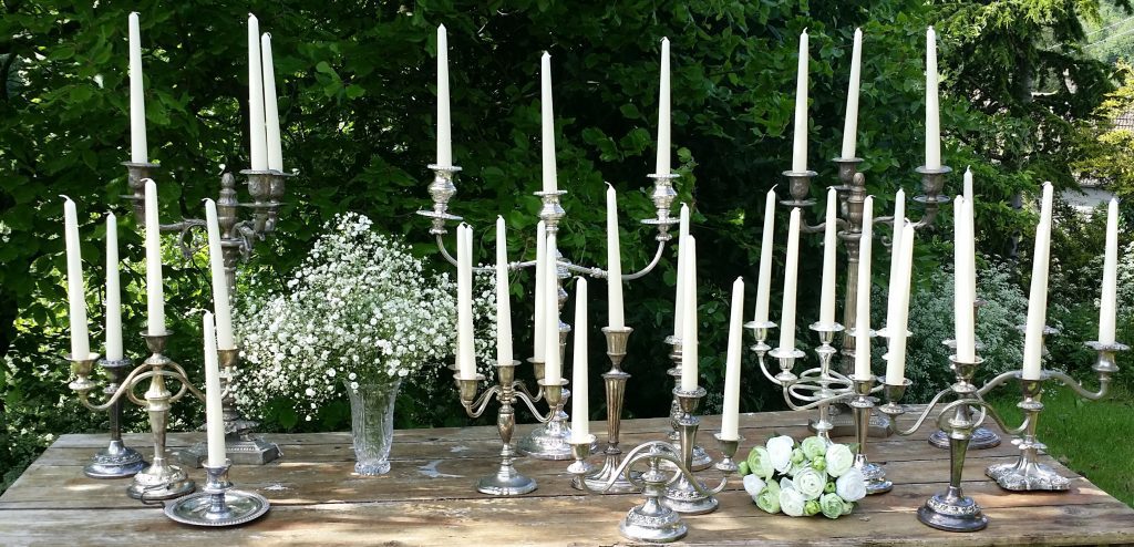 vintage silver beauty and the beast style chandeliers and candlesticks set out on a trestle table with a cut crystal vase filled with gypsophila