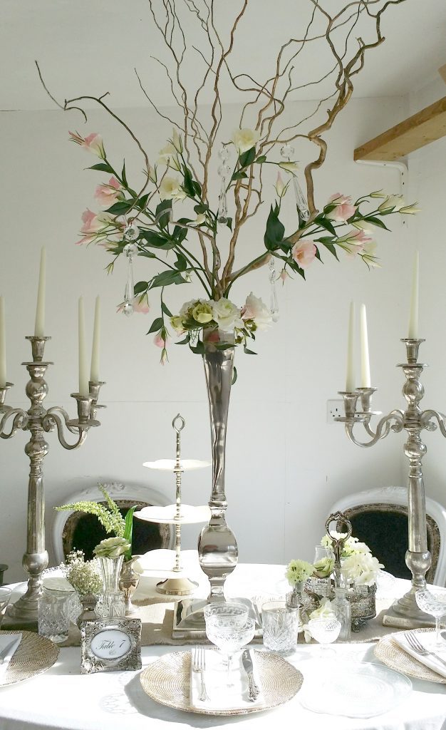 Wedding table dressing for photoshoot with cupcake cake stand silver candelabras and gold charger plates with vintage wine glasses and champagne saucers, silver picture frame table number, and a twisted willow floral arrangement in a silver vase in the centre available to hire