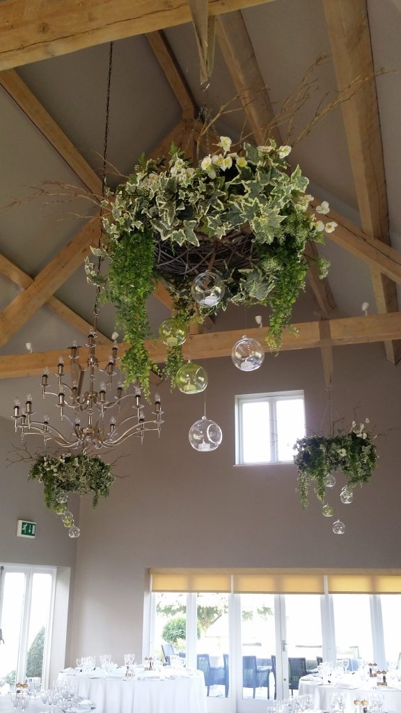 wooden wicker hanging wreath with ivy , faux flowers and glass baubles. green glass bottles in the alcoves around the room all available to hire for wedding and events and film at Frampton Barn wedding venue