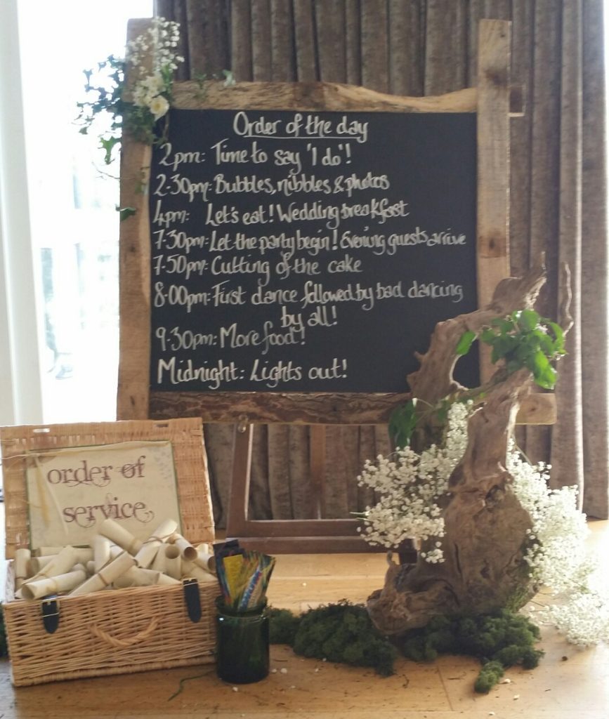 rustic wooden woodland wedding order of the day with chalkboard for DIY with scrolls for order of service, surrounded by branches moss and gypsophila- rustic order of the day to hire, as seen at Hyde Barn wedding venue