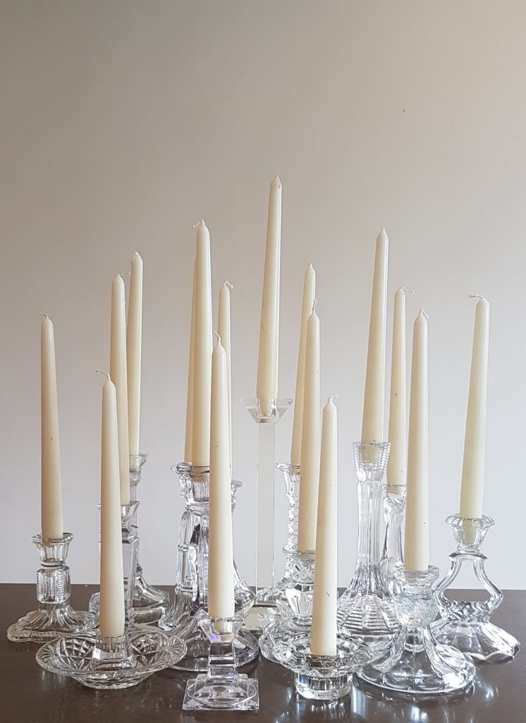 A large selection of glass candlesticks at a variety of heights and styles with a candlestick in every one