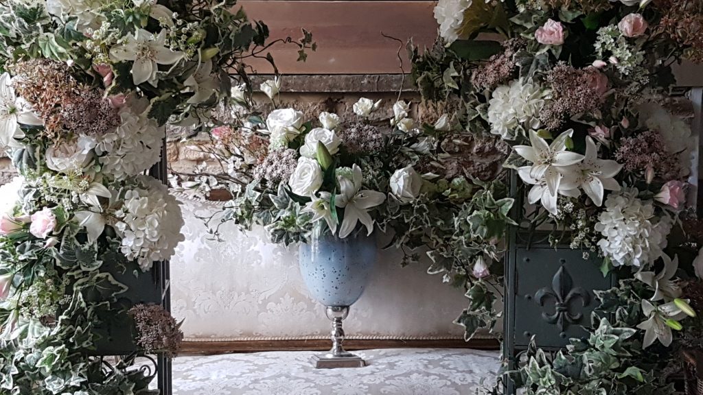 Two floral pillars of fake flowers in pinks white and greens, framing a blue glass vases on a white pedestal with the same flowers as in the pillars for hire