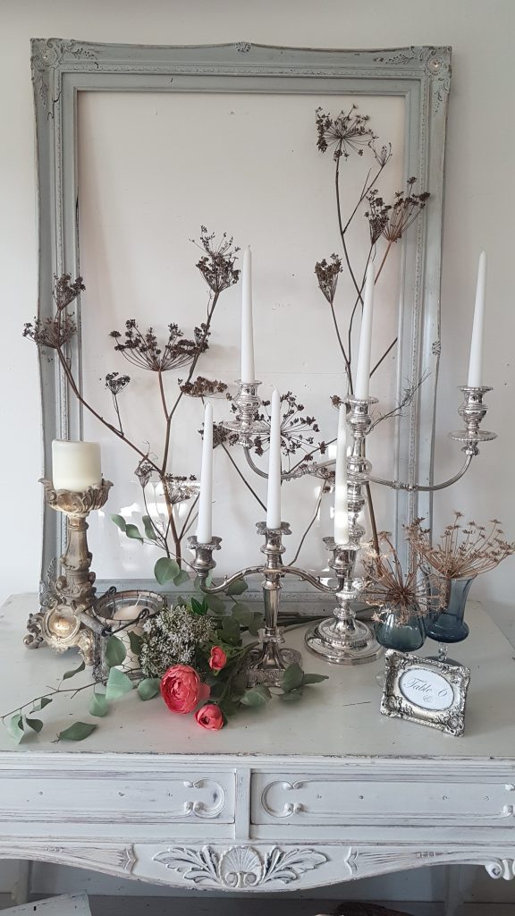 vintage silver beauty and the beast style chandeliers and Blenheim gold pillar candle sticks with coral peonies and dried flowers in front of a duck egg blue picture frame