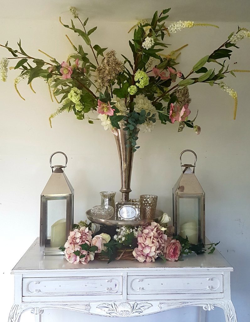 Silver Trumpet vase wedding floral centrepiece with cut crystal tealight holders and a flower arrangement with ferns, white and pink roses, white and green hydrangeas, gypsophila and white stocks with a silver lantern either side to hire