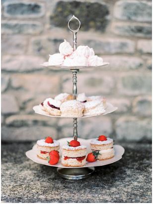 three tier ivory and silver daisy cake stand with mini victoria sponge on the bottom, scones with cream and jam in the middle and mini meringues in the top layer