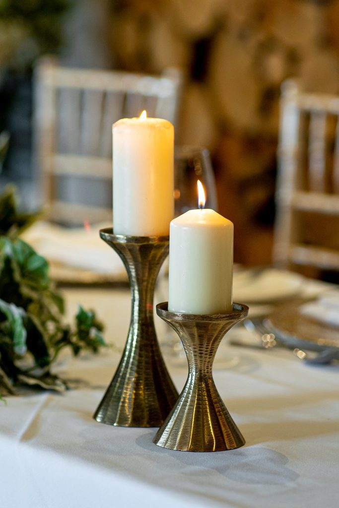 A product shot of two gold hour shaped candlesticks at different heights with a lit pillar candle on each to hire
