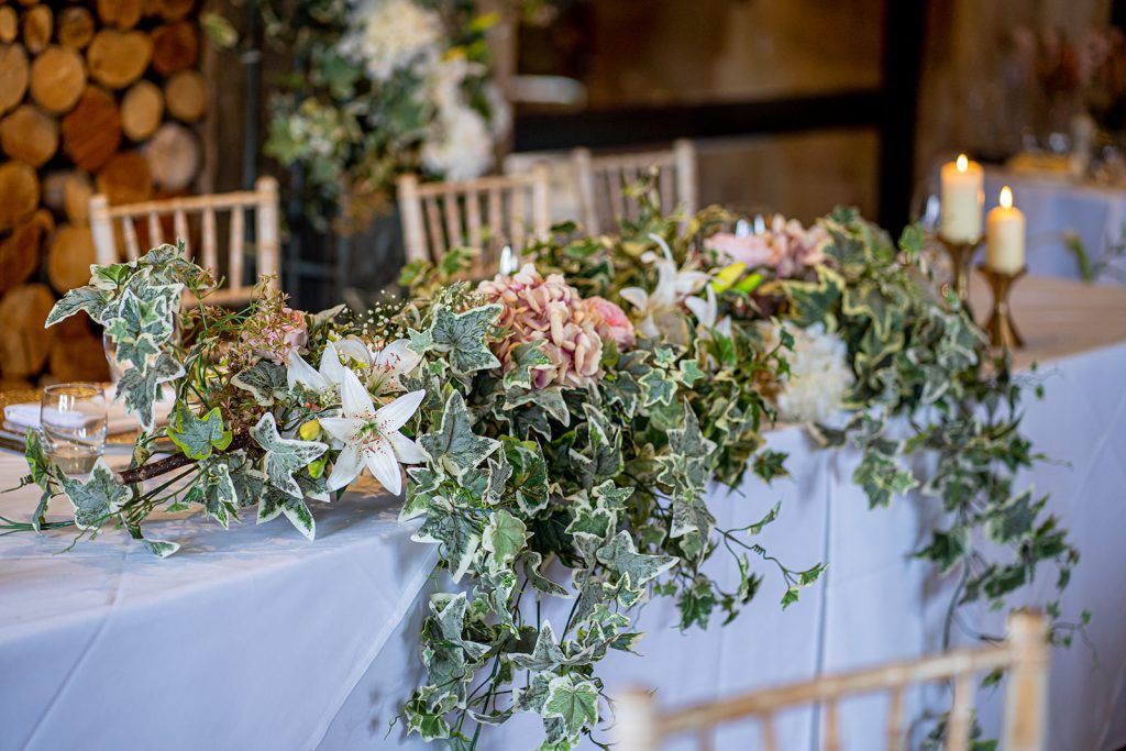 a fake flower garland arrangement on the top table with green and white ivy and with pink hydrangea heads and white lilies for hire