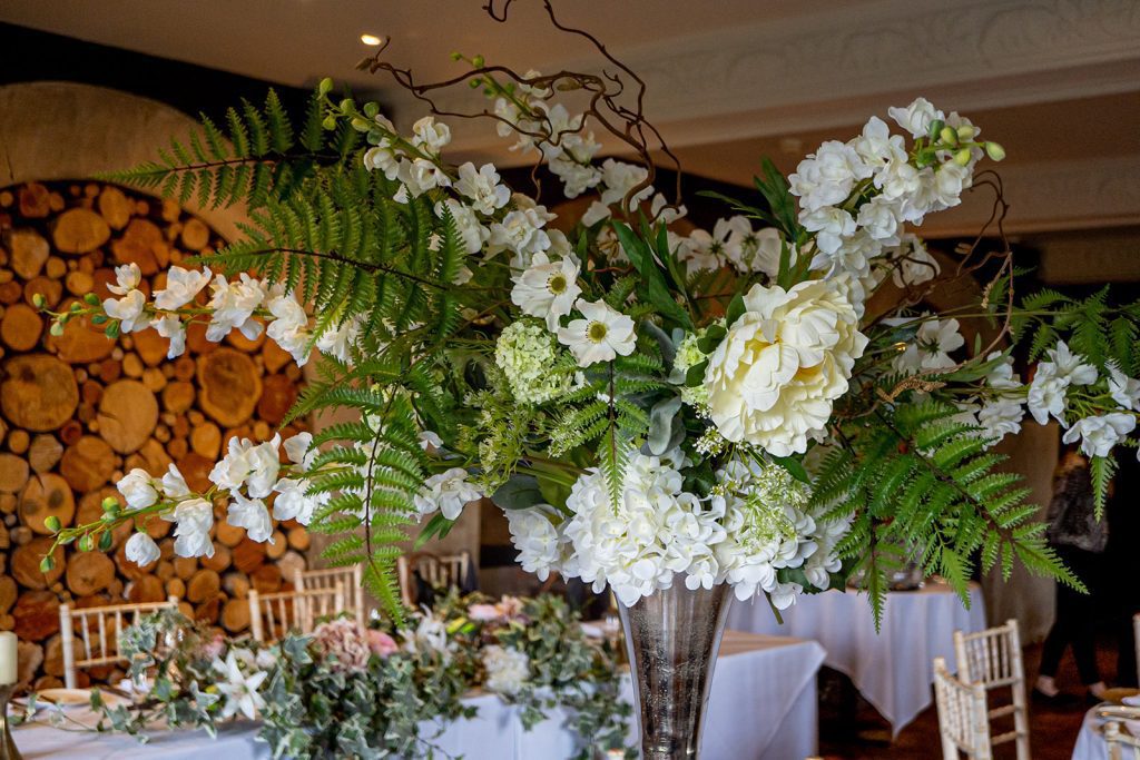 Silver Trumpet vase wedding floral centrepiece with a flower arrangement with ferns, white and pink roses, white and green hydrangeas, gypsophila and white stocks as w round table centrepiece with cut glass charger plates and a classic diner set complete with wine and water glasses and cutlery to hire