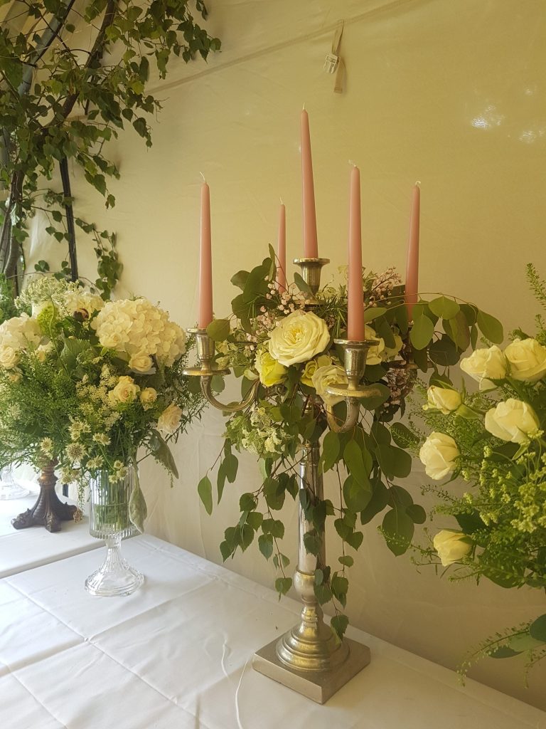 Trestle tables under a stretch tent marquee with our rustic silver candelabras with pink candle sticks with crystal vases filled with fresh flowers and foliage