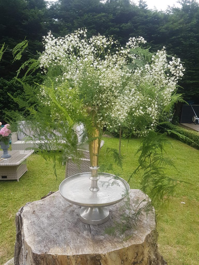 Stunning large silver trumpet vase filled with ferns and gypsophila sat on a huge cut down tree trunk