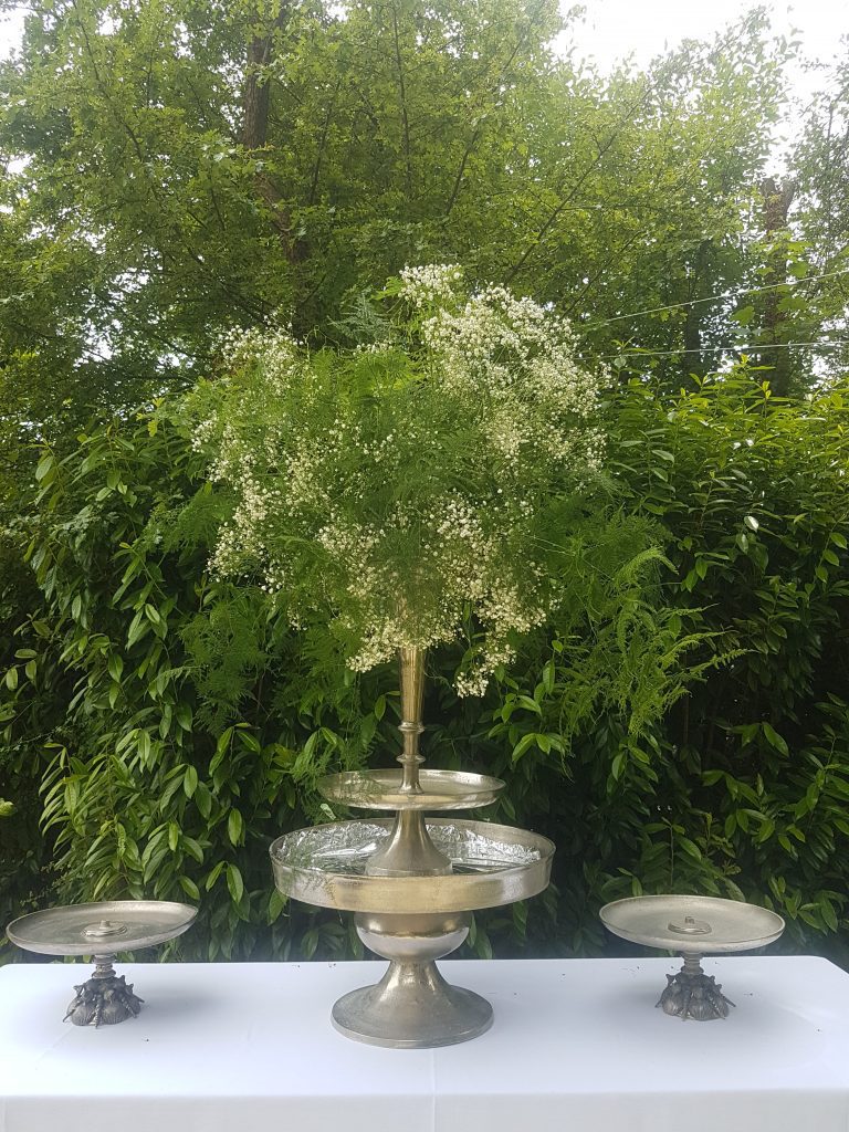Stunning large silver trumpet vase filled with ferns and gypsophila on a huge silver cake stand with two smaller silver cake stands either side