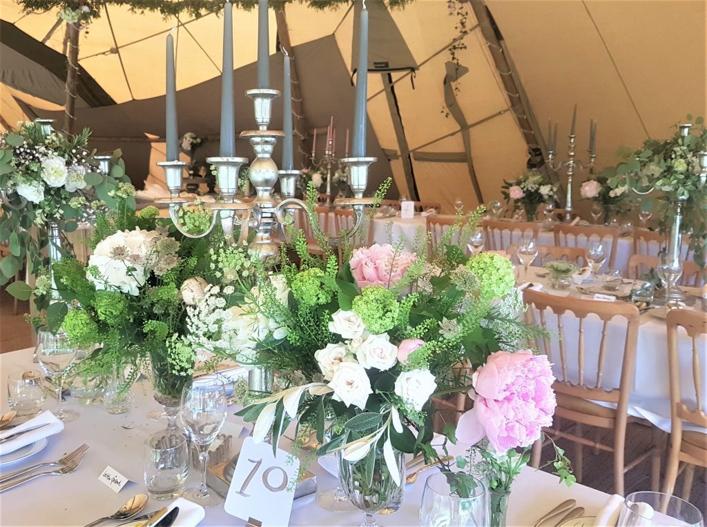Trestle tables under a stretch tent marquee with our rustic silver candelabras with pink and taupe candle sticks with crystal vases filled with fresh flowers and foliage