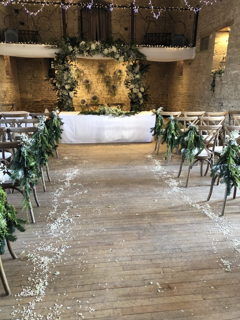 ceremony set up at the great tythe barn in Tetbury with a faux floral arch and fresh greenery