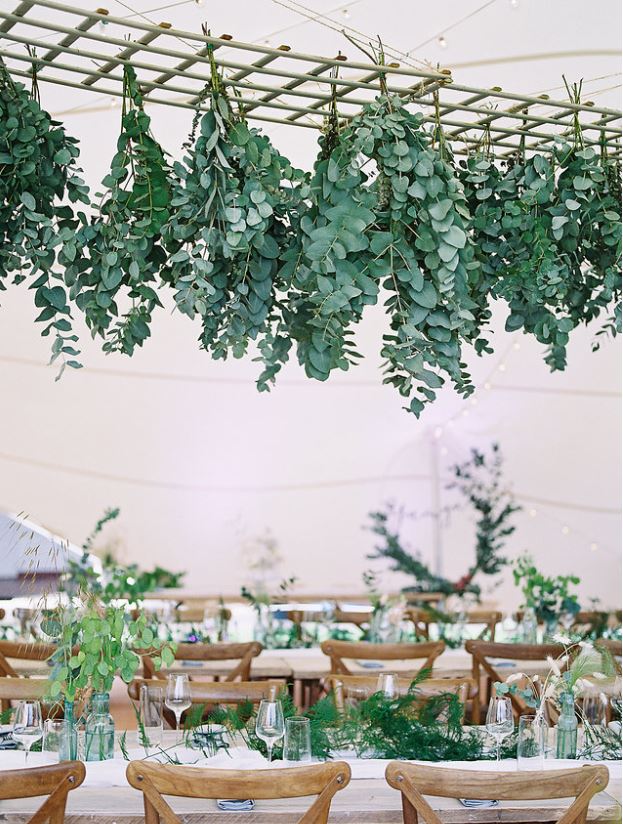 aqua green and clear glass bottles on trestle tables at marquee wedding with fake eucalyptus hanging from above for hire