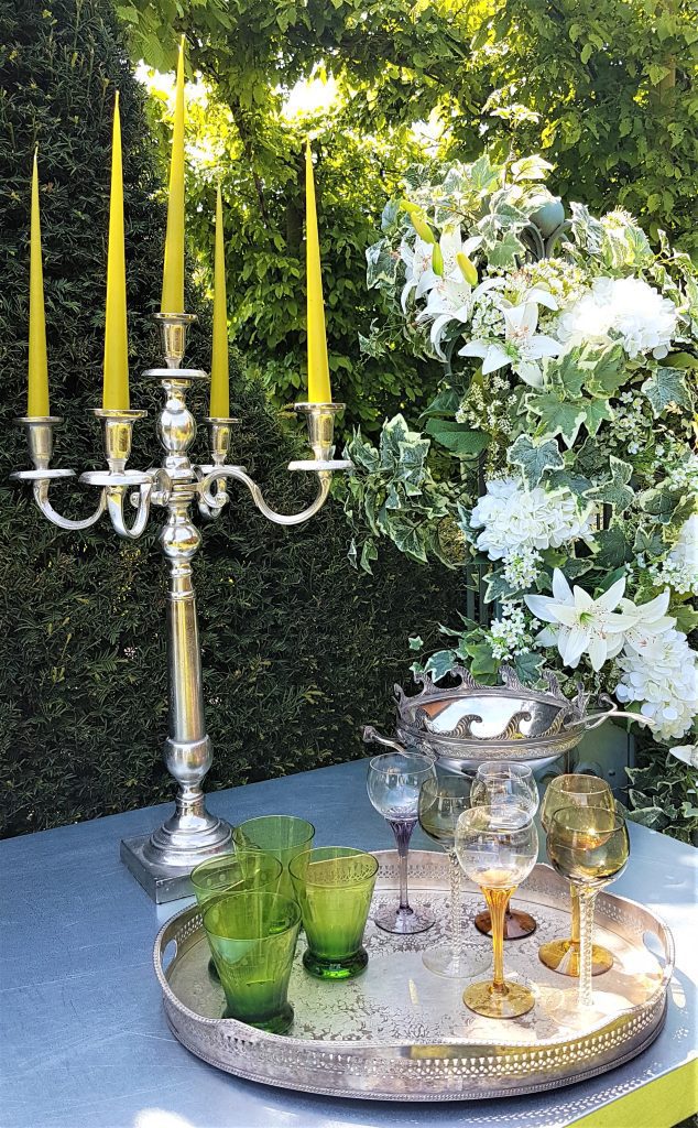 Case iron silver five spoke candelabra with lime green candles next to a silver vintage tray with coloured stem wine glasses and green water tumblers with a faux flower floral pillar behind to hire