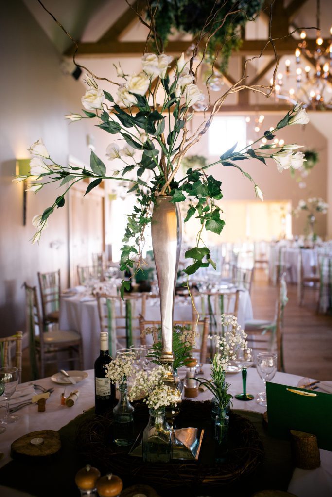 Large lisianthus and twisted willow silver vase centrepiece, with recycled glass bottles and gypsophila on a log round and log tealight holders to hire