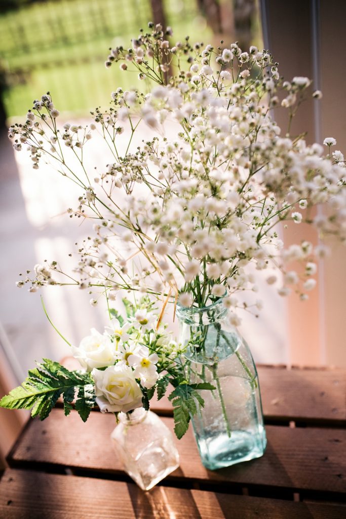 mixed old glass bottles with white roses and gypsophila to hire for woodland flowers at weddings, events, parties and films