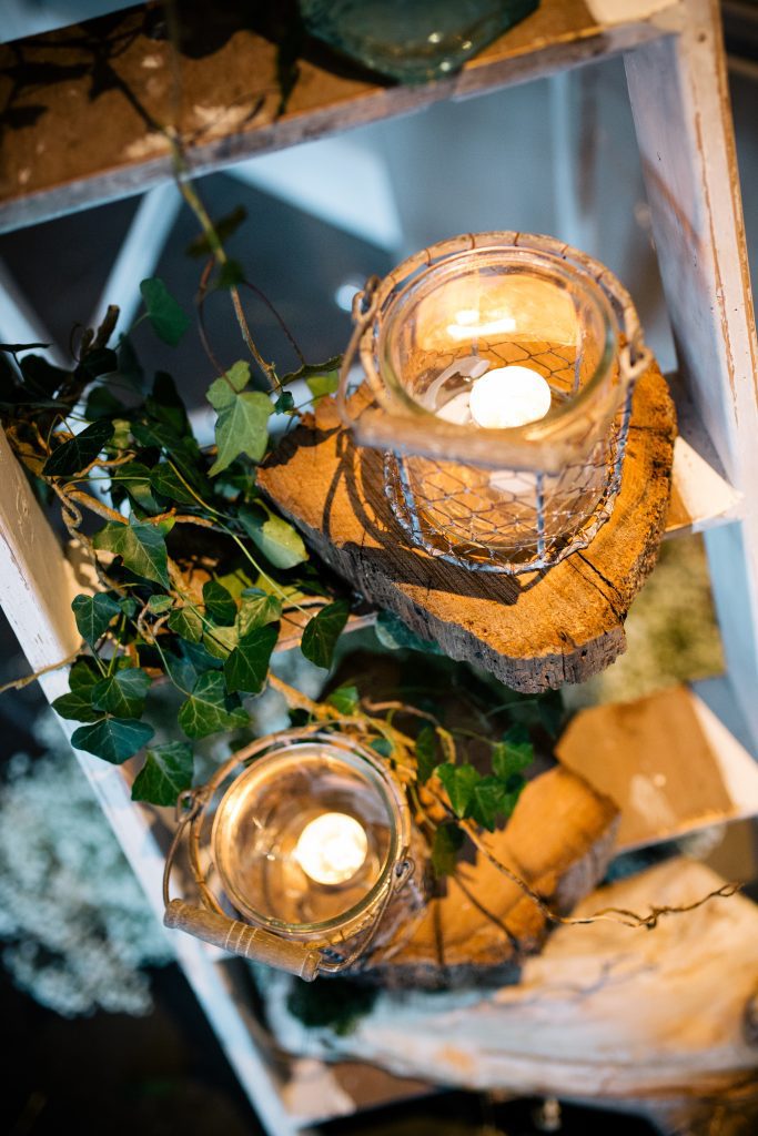 Rustic chicken wire candle or flower holders with a glass vase and wooden handle with lit candles on a wooden ladder twisted with ivy at Hyde barn available to hire for weddings and events
