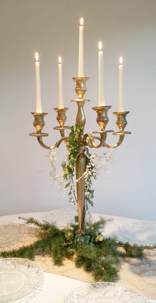 Gold candelabra with ivy wrapped around it and a string of pearl draped over the arms and pine branches placed around the base to hire