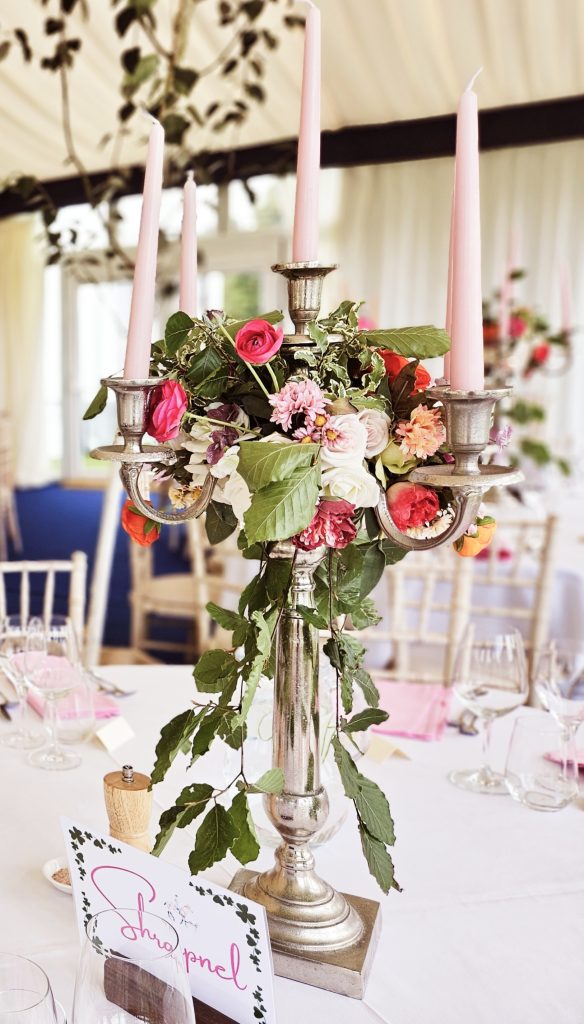 Centrepiece of a silver candelabra with a wreath of bright pink and orange roses and fresh beech trailing from the centre and pink candles for hire