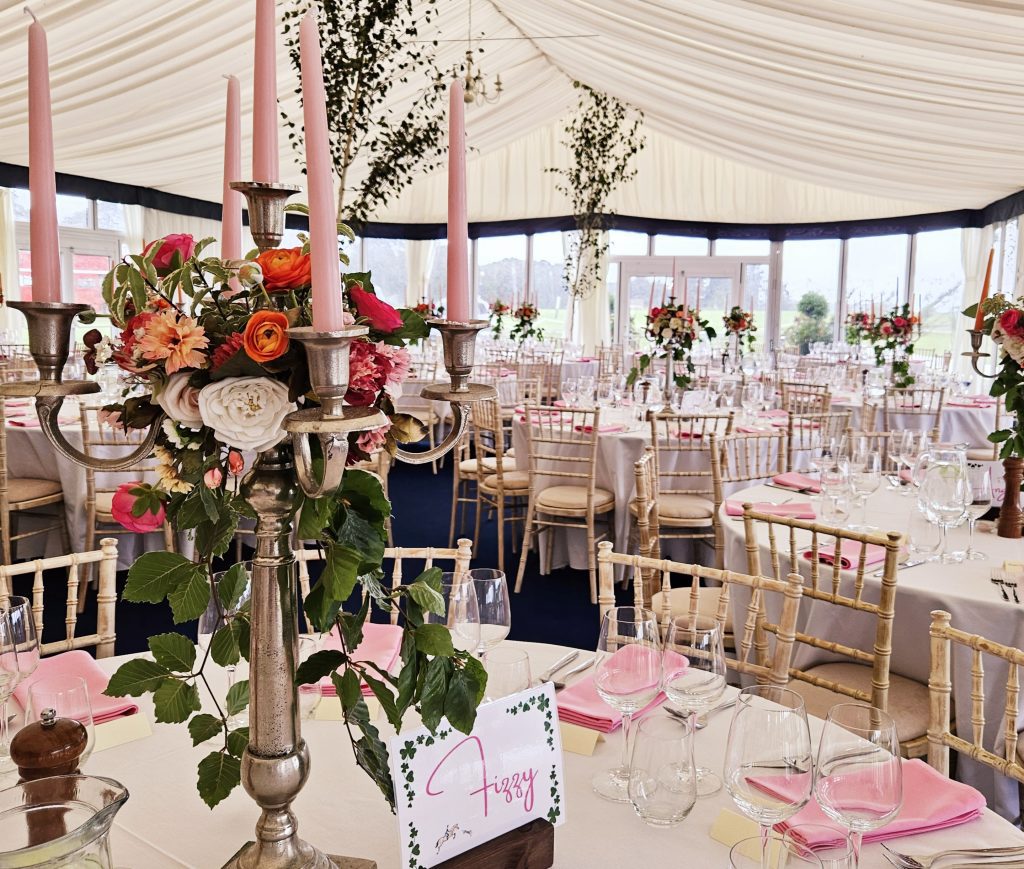 In the marquee at Beaufort polo club in the Cotswolds Centrepiece of a silver candelabra with a wreath of bright pink and orange roses and fresh beech trailing from the centre and pink candles for hire