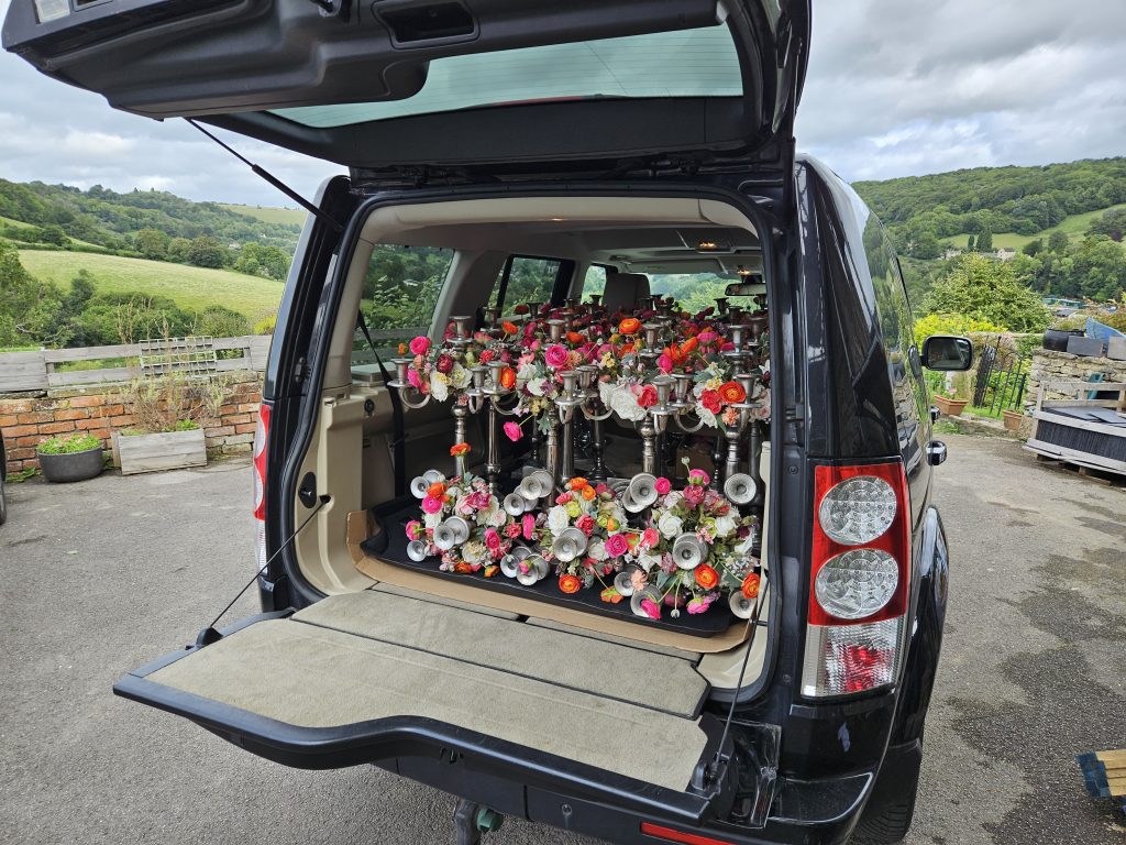 A land rover discovery 4 packed with silver candelabras with wreaths of orange and pink ranunculi for a marquee wedding at Beaufort polo club in the Cotswolds for hire