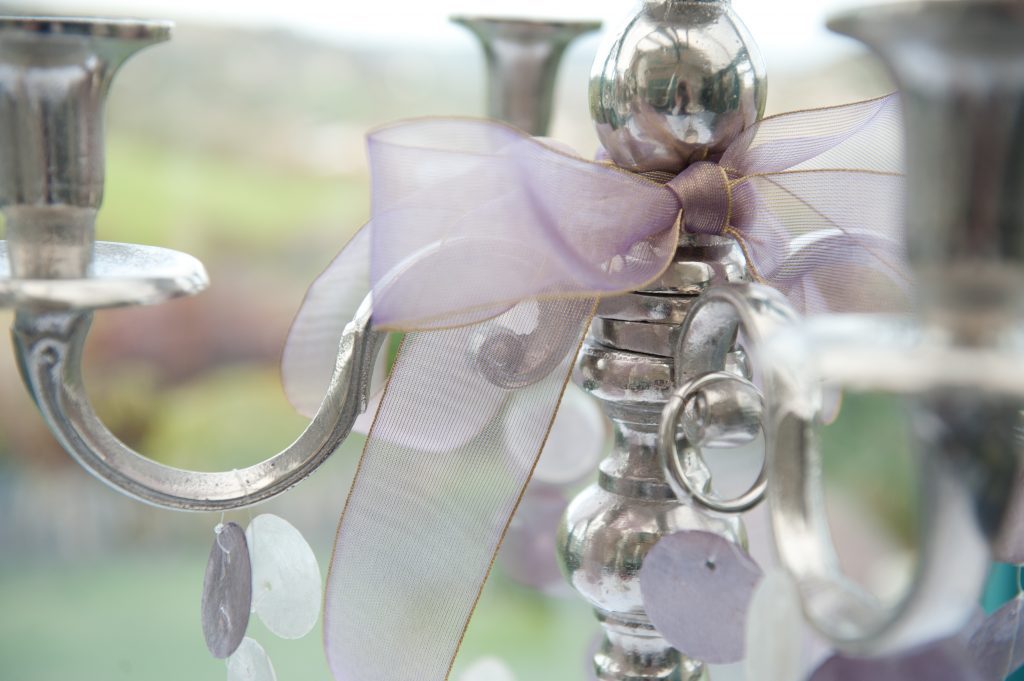 Close up of a silver candelabra with a purple organza with a gold trim and pearlized discs hanging on the arms