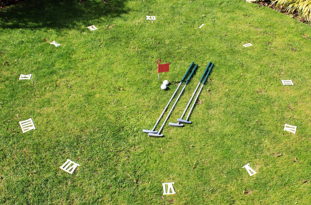 Clock golf, an outdoor garden game set up on the lawn with four putters and two golf balls in the centre by the red flag