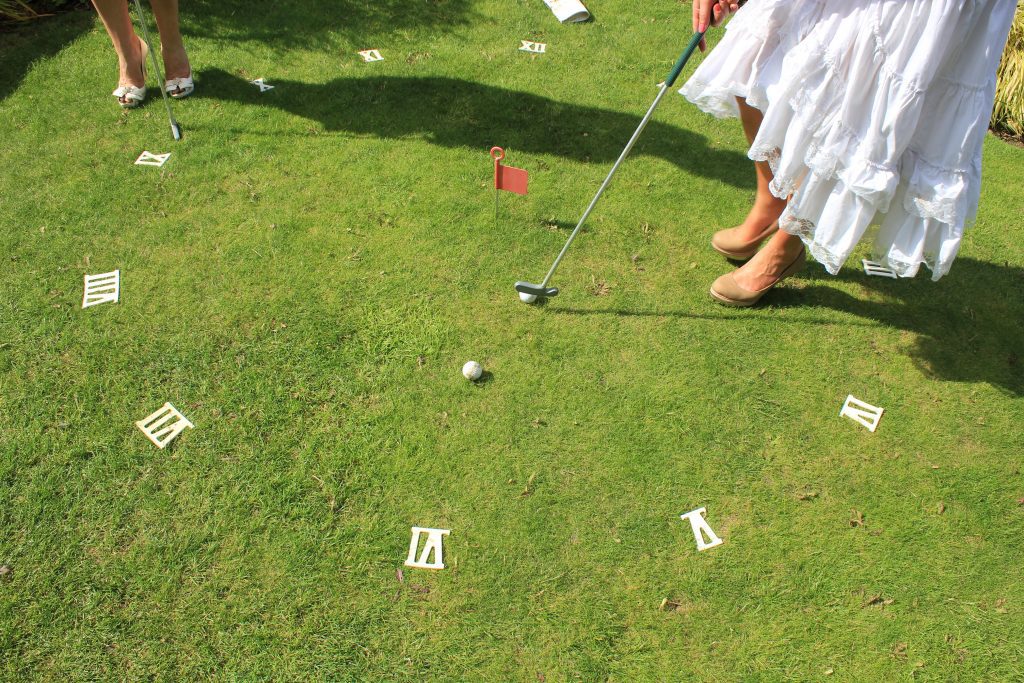 Clock golf, an outdoor garden game set up on the lawn with four putters and two golf balls in the centre by the red flag