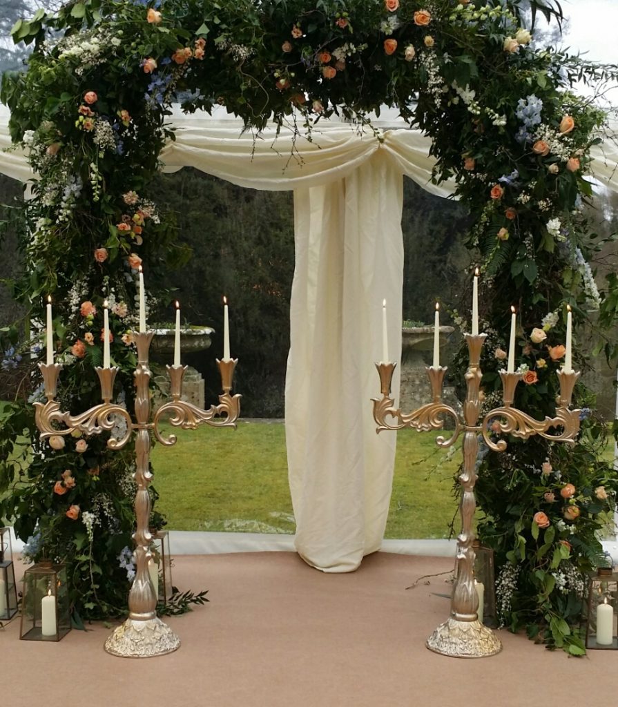 Two Stunning ornate extra large candelabras with pillar candles in front if a large floral arch and glass lanterns around the base for hire