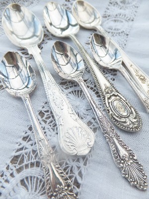 Vintage ornate silver teaspoons on a lace tablecloth available to hire