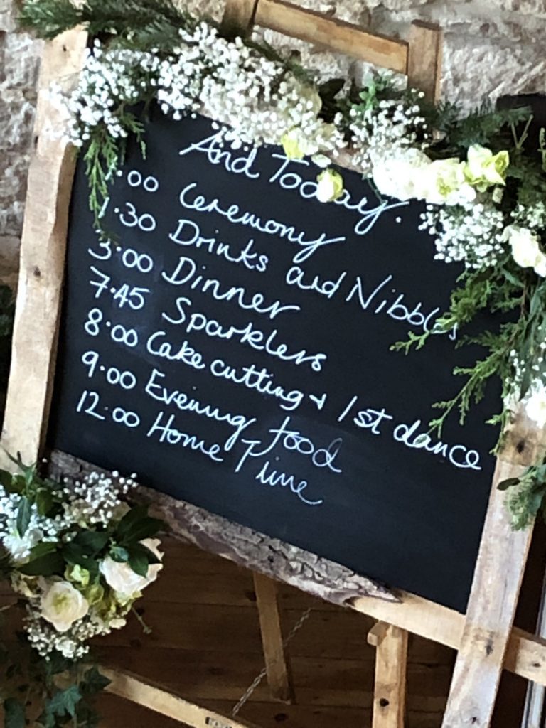 rustic wooden woodland wedding order of the day with chalkboard for DIY with scrolls for order of service, surrounded by branches moss and gypsophila- rustic order of the day to hire, as seen at Hyde Barn wedding venue for hire