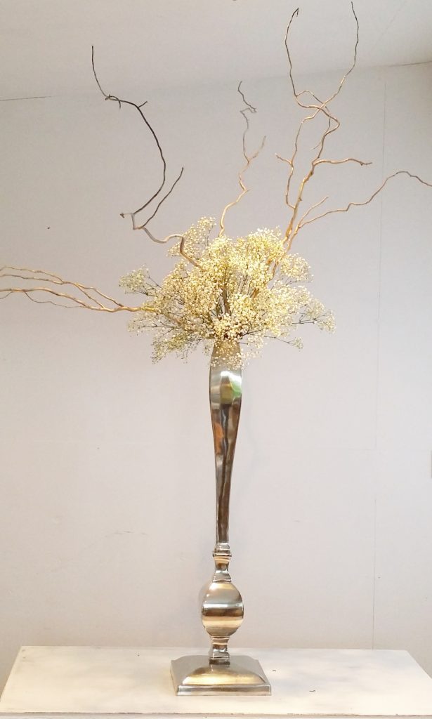 tall elegant wedding table centerpiece decoration of a high shine silver candelabra transformed into a vase like piece with an arrangement of gypsophila and twisted willow