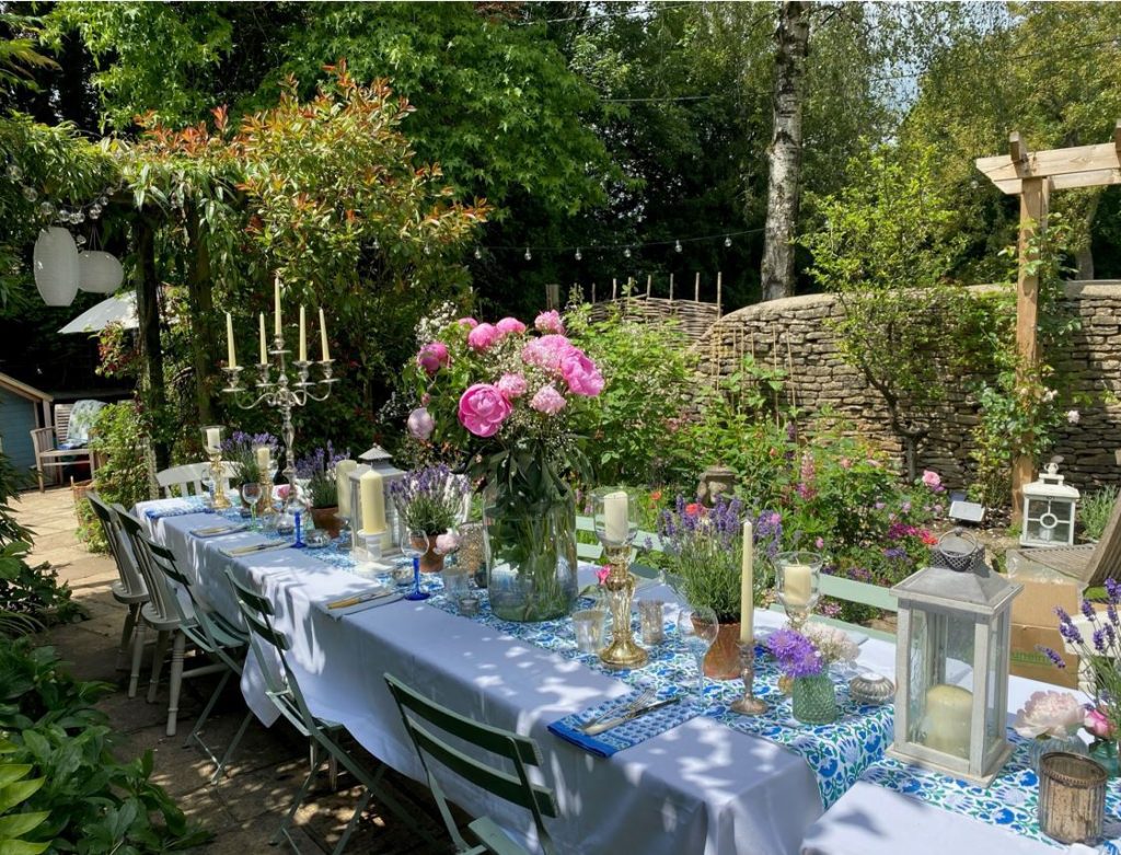 Summer garden party Trestle table with a blue runner and a variety of gold candelabras gold glass goblet tealight holders and fresh lavender, gypsophelia and pink roses in coloured vases with bone handle knives and forks available to hire