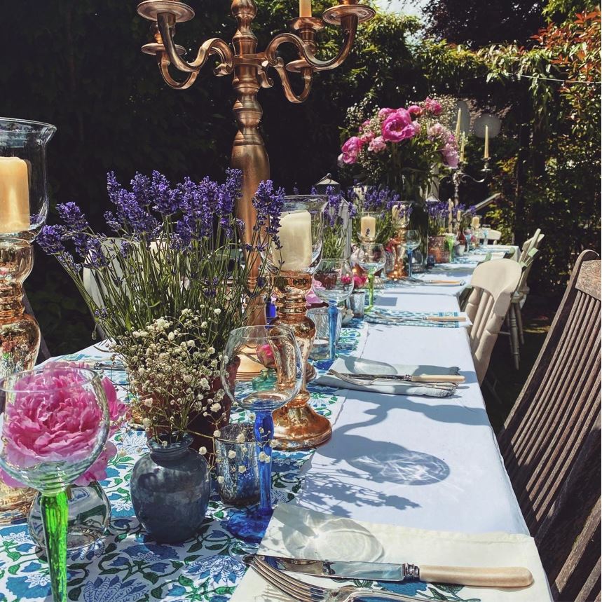 Summer garden party Trestle table with a blue runner and a variety of gold candelabras gold glass goblet tealight holders and fresh lavender, gypsophelia and pink roses in coloured vases with bone handle knives and forks available to hire