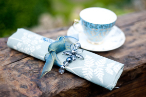 blue vintage teacup and saucer with a blue fern printed napkin tied with a blue ribbon and blue beads for hire