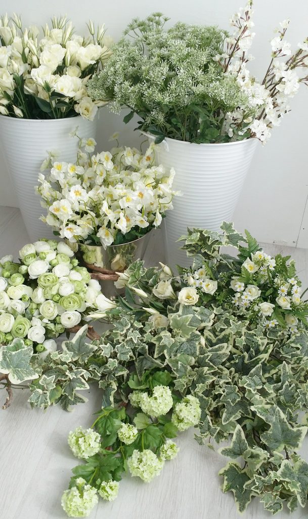 Luxury quality faux flowers in whites and greens, spring blossom, lisianthus, asparagus fern, roses, peonies and ivy, displayed on the floor in large white buckets