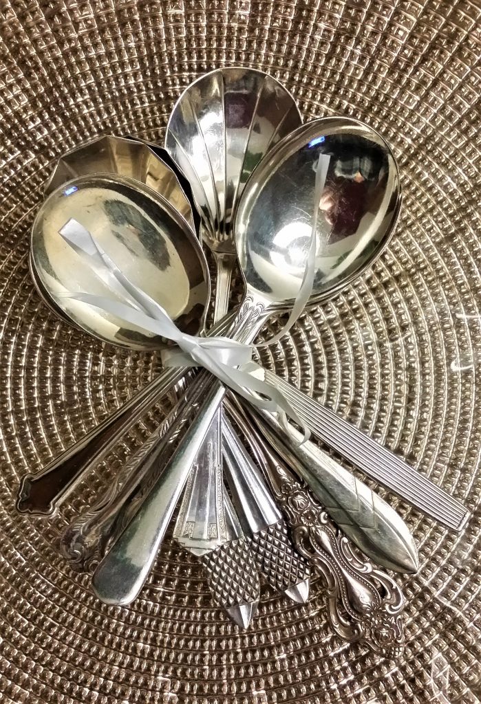 A bunch of silver vintage soup spoons on a gold charger plate available to hire