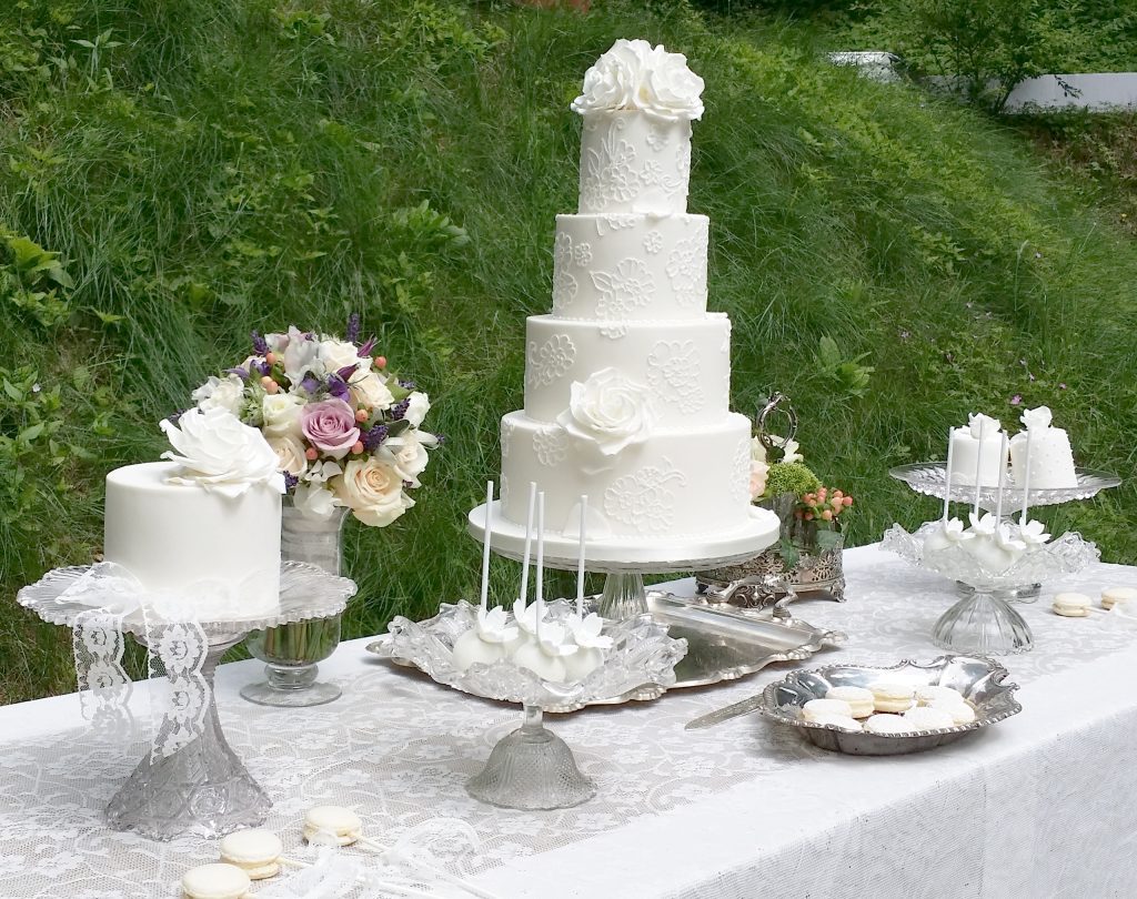 glass pedestal wedding cake stands with different styles and shapes and sizes for mix and match or a sweet station and a grand four tier white wedding cake in the centre on a silver vintage tray for hire