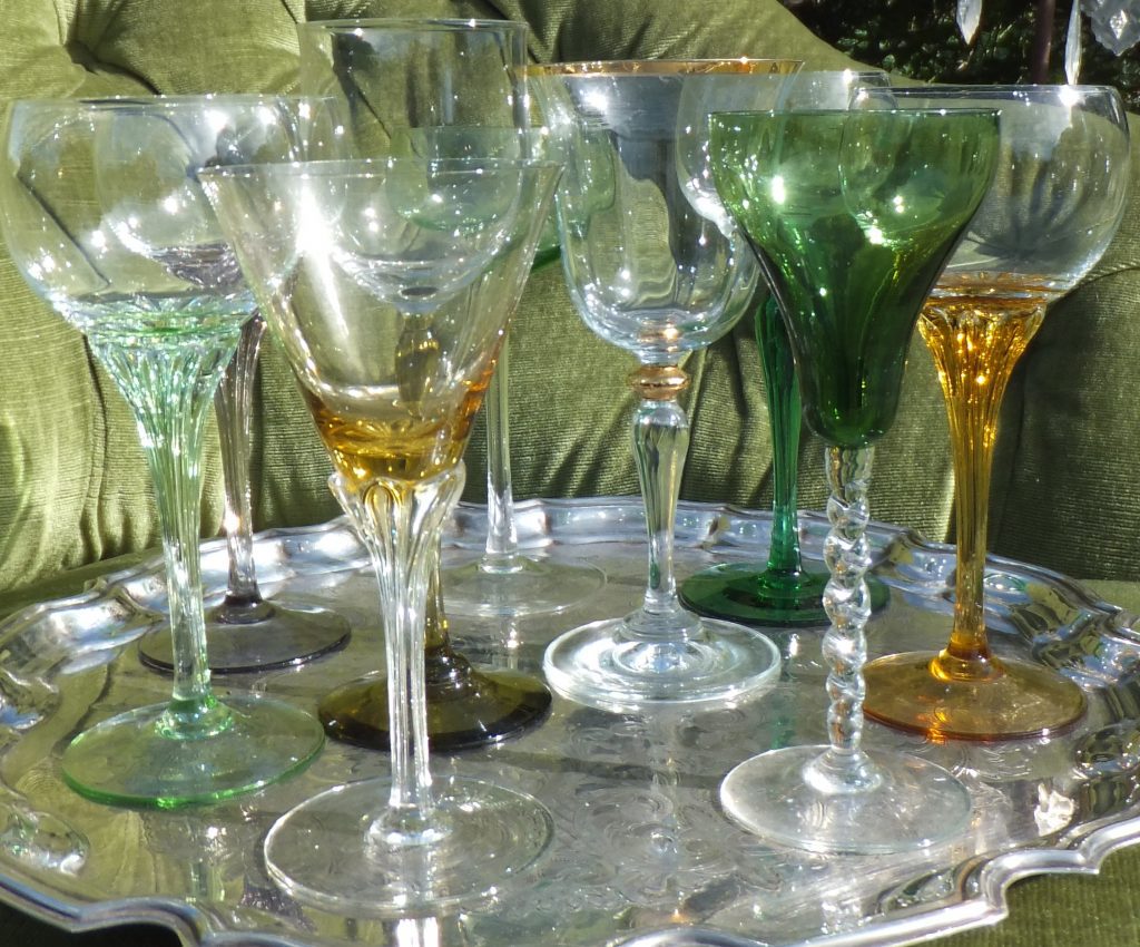 A silver tray of coloured wine glasses sat on a green velvet vintage sofa for hire