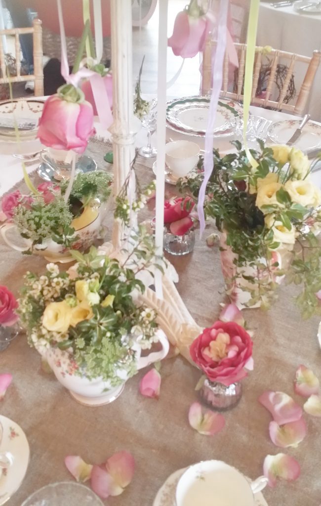 close up of a table centrepiece base on a hessian table cloth with vintage tea pots and bud vases filled with fresh spring flowers for hire