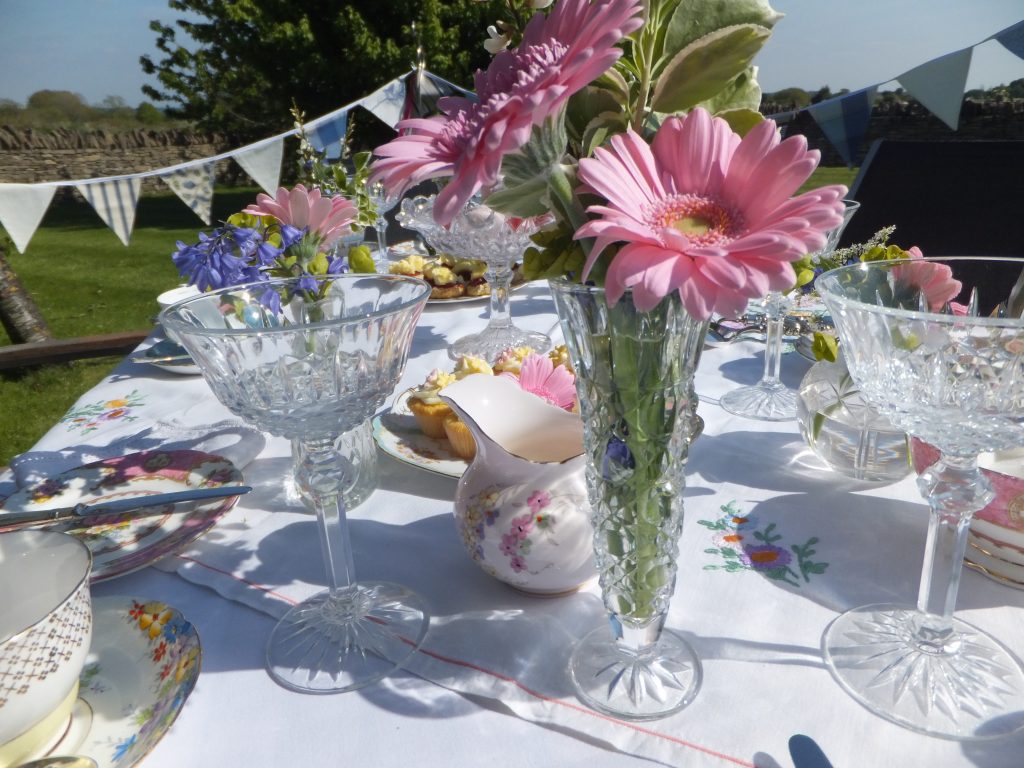 a garden party hen do table set up with luxury bunting an vintage china and champagne saucers with cut crystal vases filled with pink gerberas and greenery