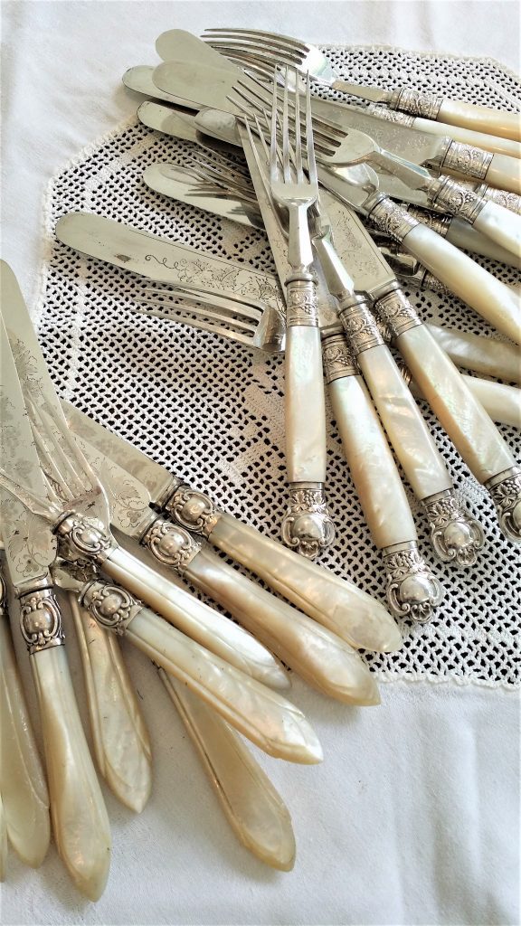 Vintage silver cutlery with ivory handles and ornate silver details in bunches of knives and forks on a white lace tablecloth