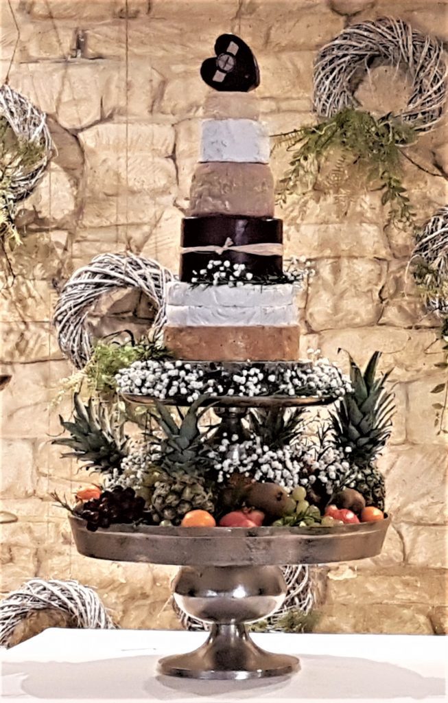 a grand layered three tiered silver cake stand. The bottom and middle layers are filled with grapes, peaches, apples and pears the top layer is a 8 tier cake built of different cheeses all available to hire