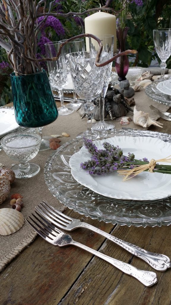 Cut glass charger plate to hire with a hessian runner and sea shell cake stands with bunches of lavender on white vintage plates to hire