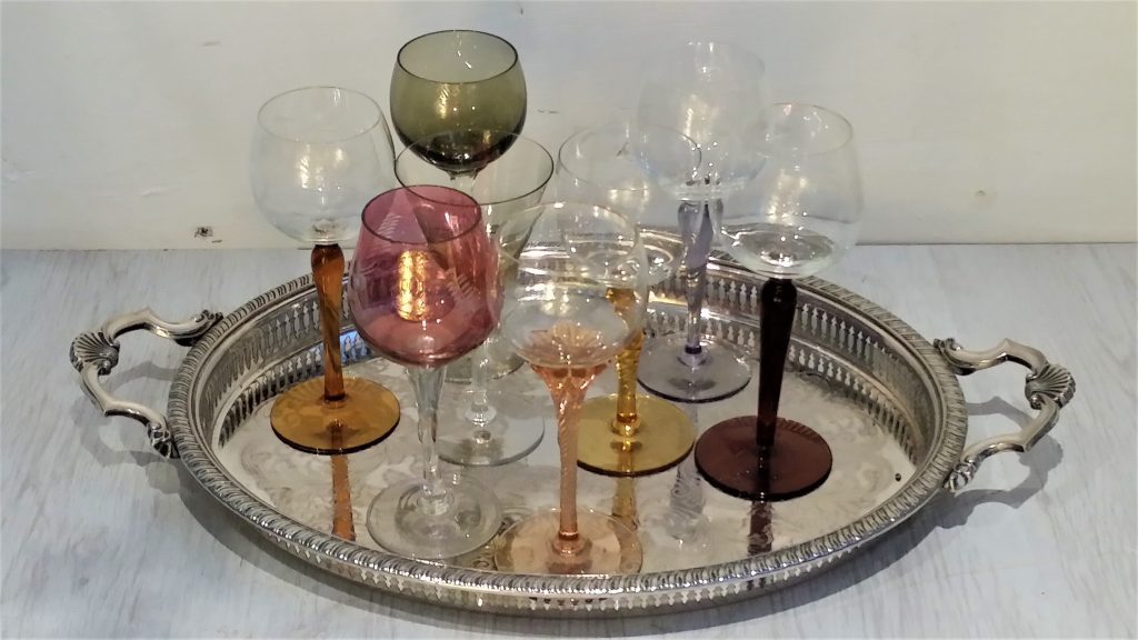 A vintage silver patterned tray with seven wine glasses in autumnal oranges purples and pinks some with clear stems some with coloured