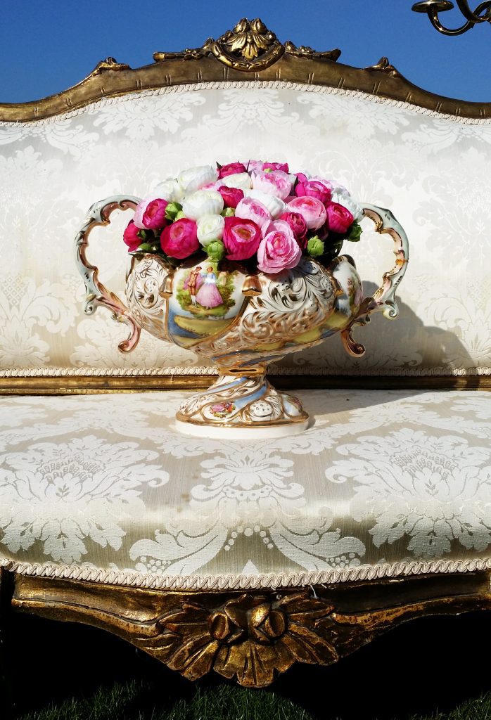 Close up of white stylish vintage sofa with gold with a silver vase sat in the centre filled with pink and white faux flowers