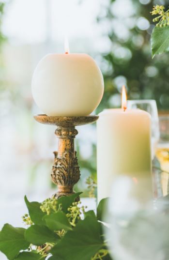a close up of a pillar candle and a round ball candle lit on rococo gold ornate candlesticks with green ivy around the base
