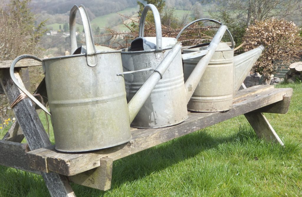 three grey metal watering cans on a bench for hire